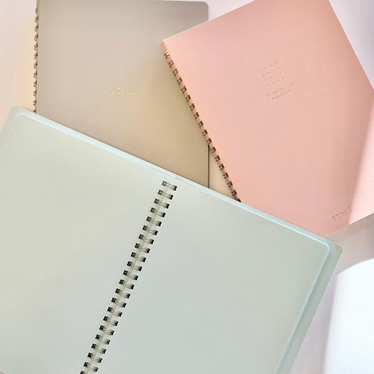 Three notebooks in pastel colors on a light pink background