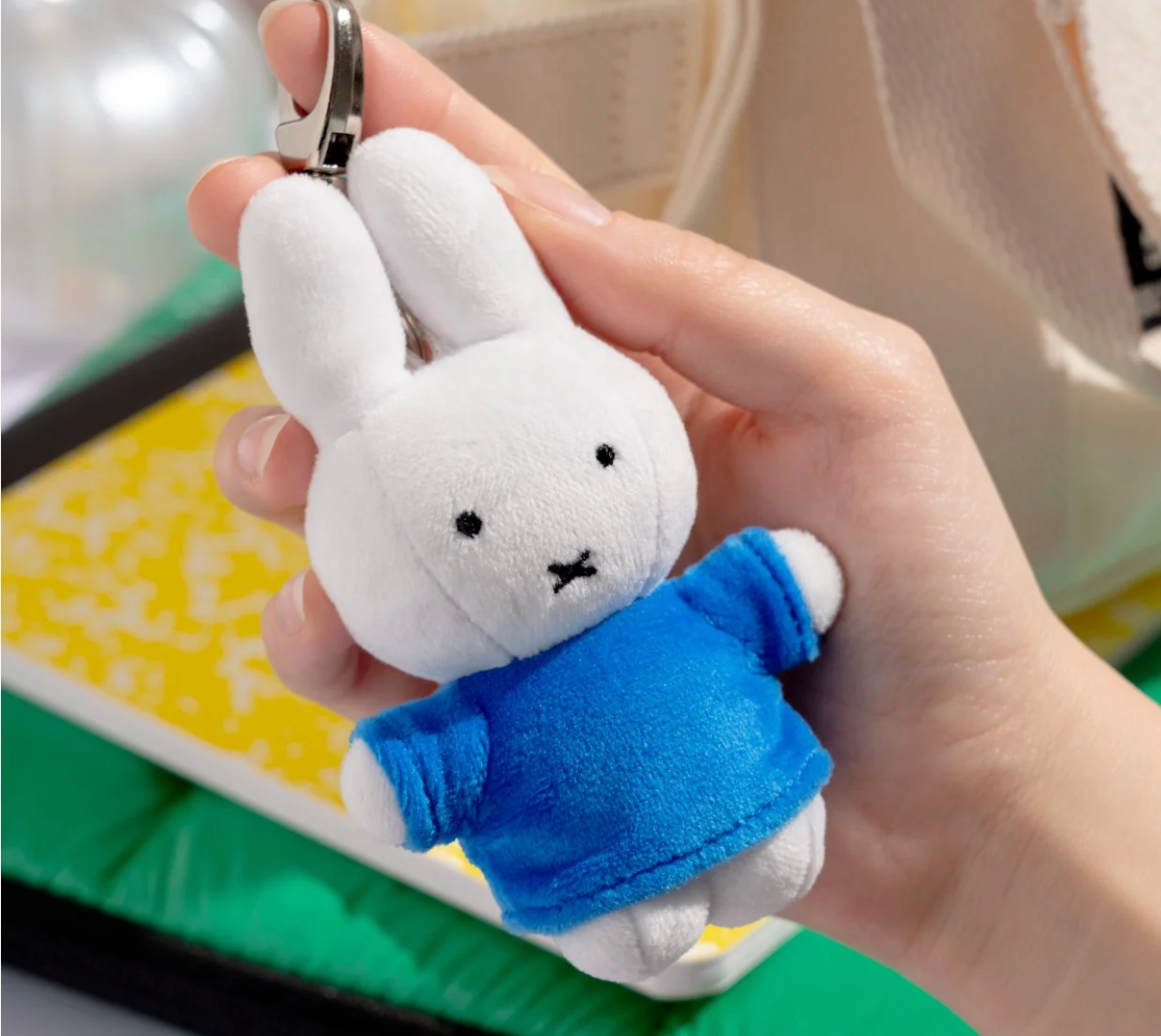 Plush rabbit keychain with a blue sweater held in a hand against a blurred background