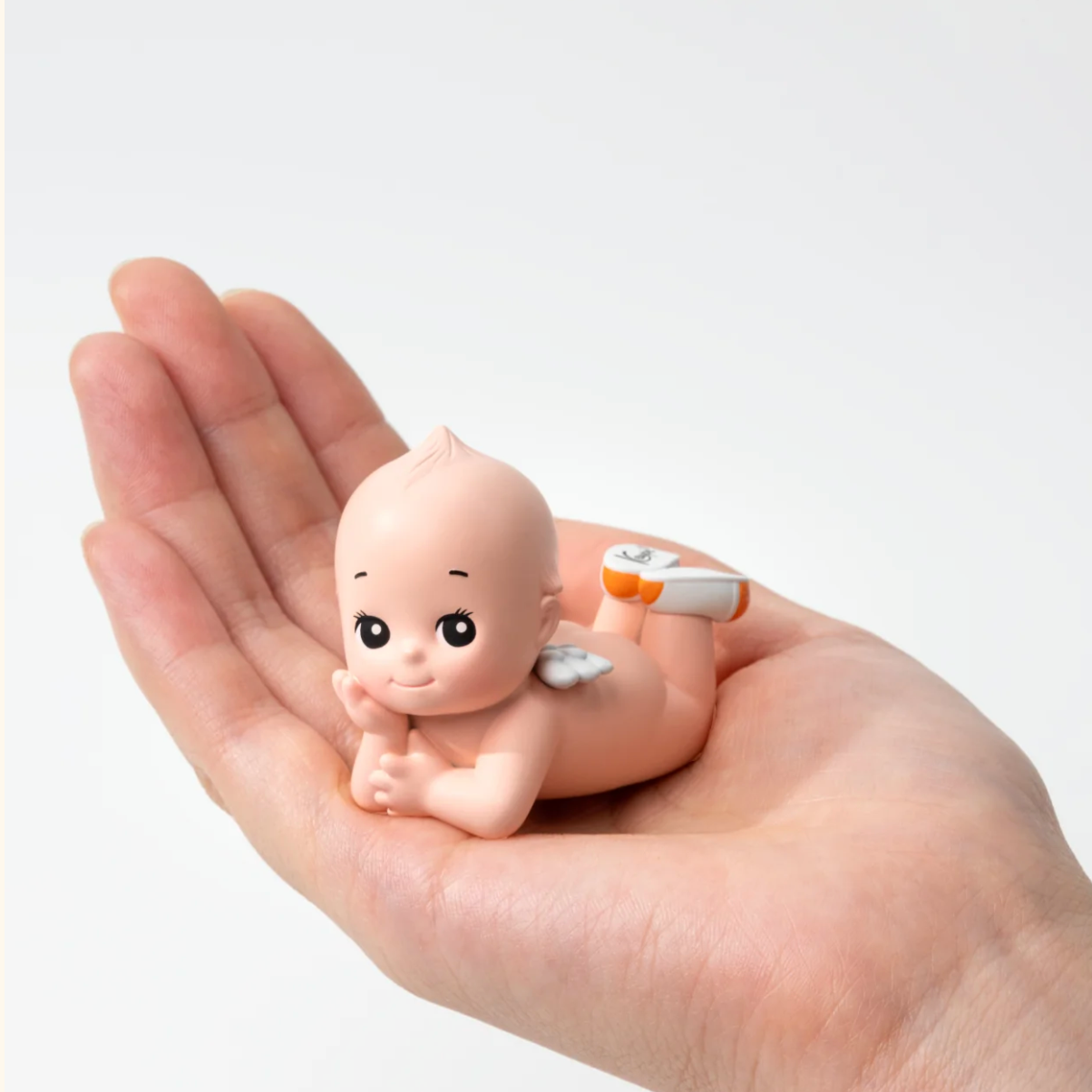 Small baby figurine held in a hand against a white background