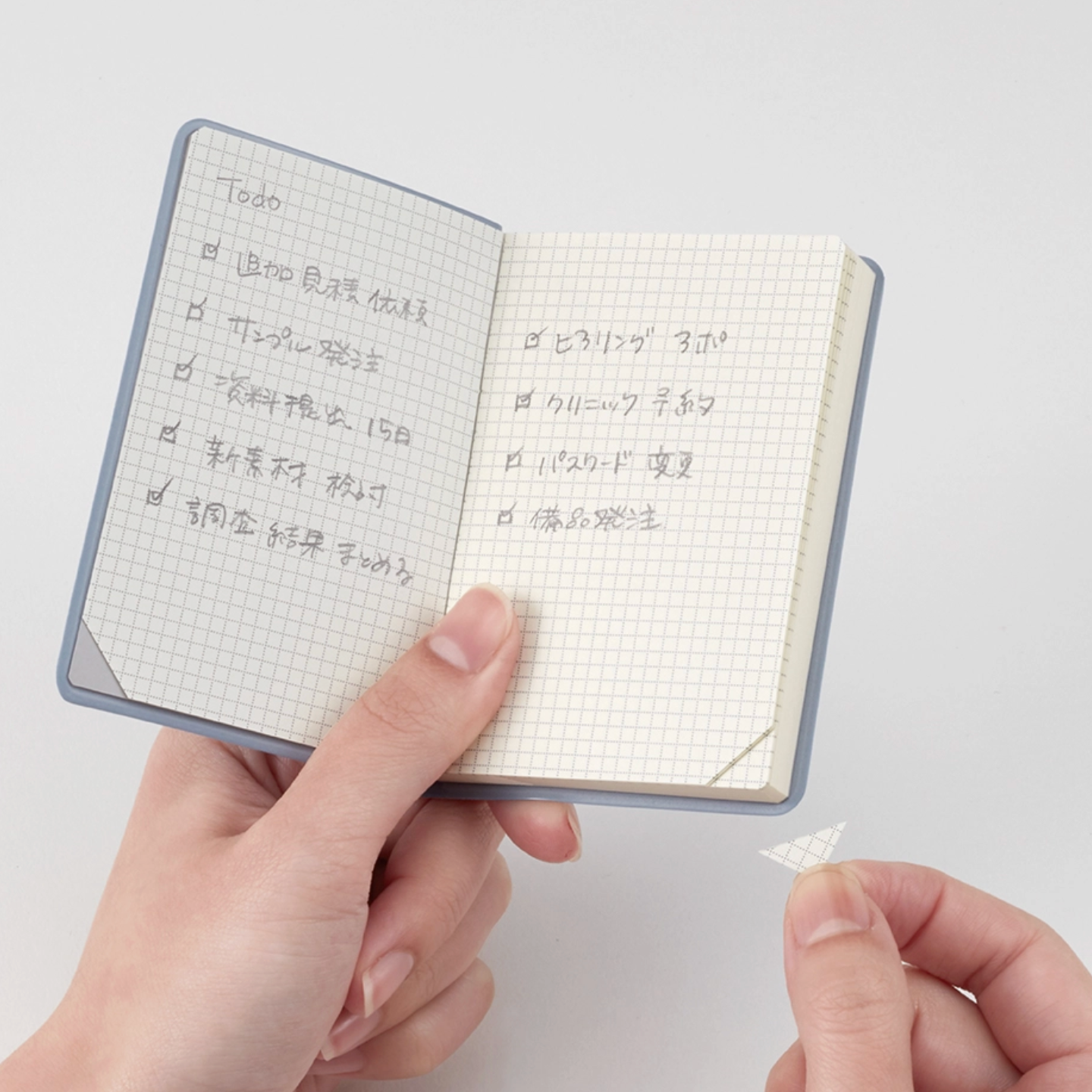 Small notebook with grid pages held by a hand on a light gray background