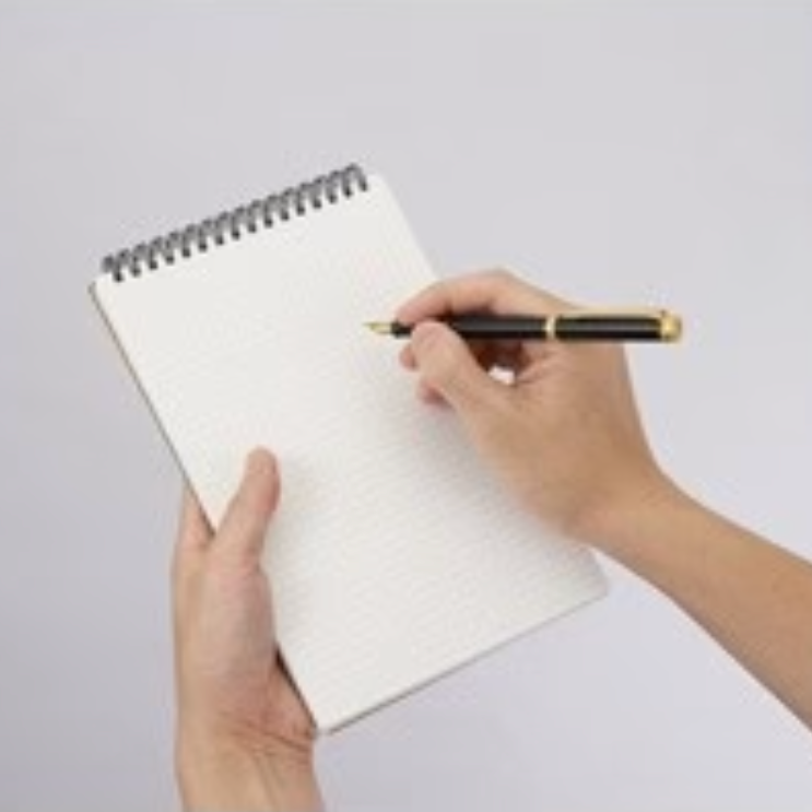 Hand holding a pen poised over a blank notebook on a light gray background
