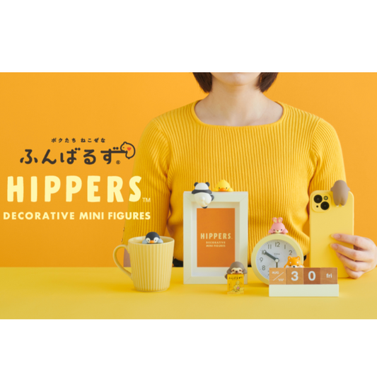 Person holding a phone with a HIPPERS decorative mini figure, surrounded by other HIPPERS products on a yellow background.