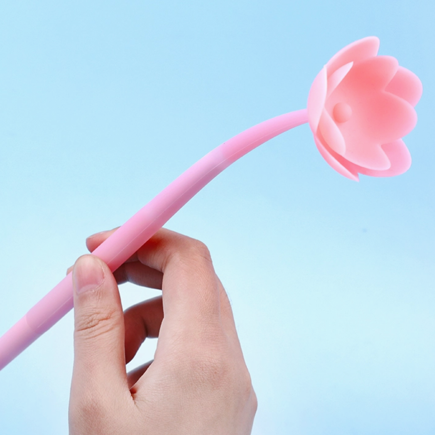 Hand holding a pink straw with a flower-shaped top against a light blue background