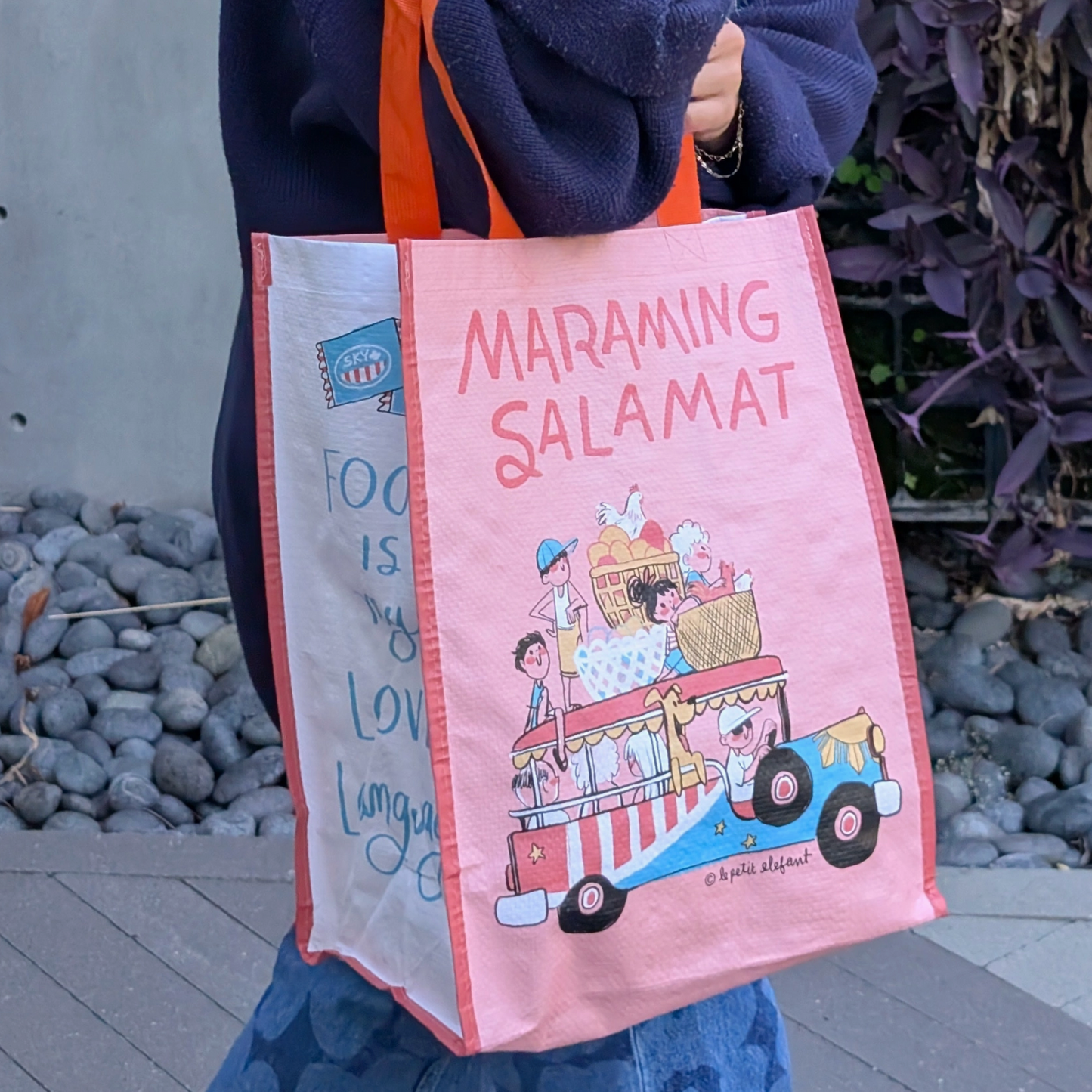 Person holding a pink tote bag with cartoon design and text.