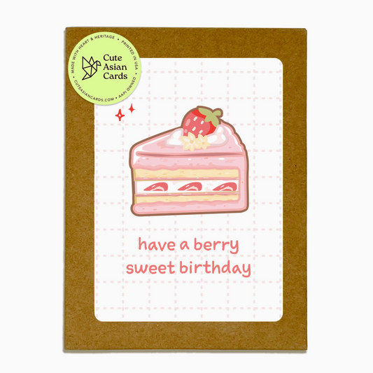 A square greeting card with a brown kraft envelope-style border and a white center panel featuring an illustration of a pink strawberry cake and the text 'have a berry sweet birthday.' A round green sticker at the top left reads 'Cute Asian Cards.