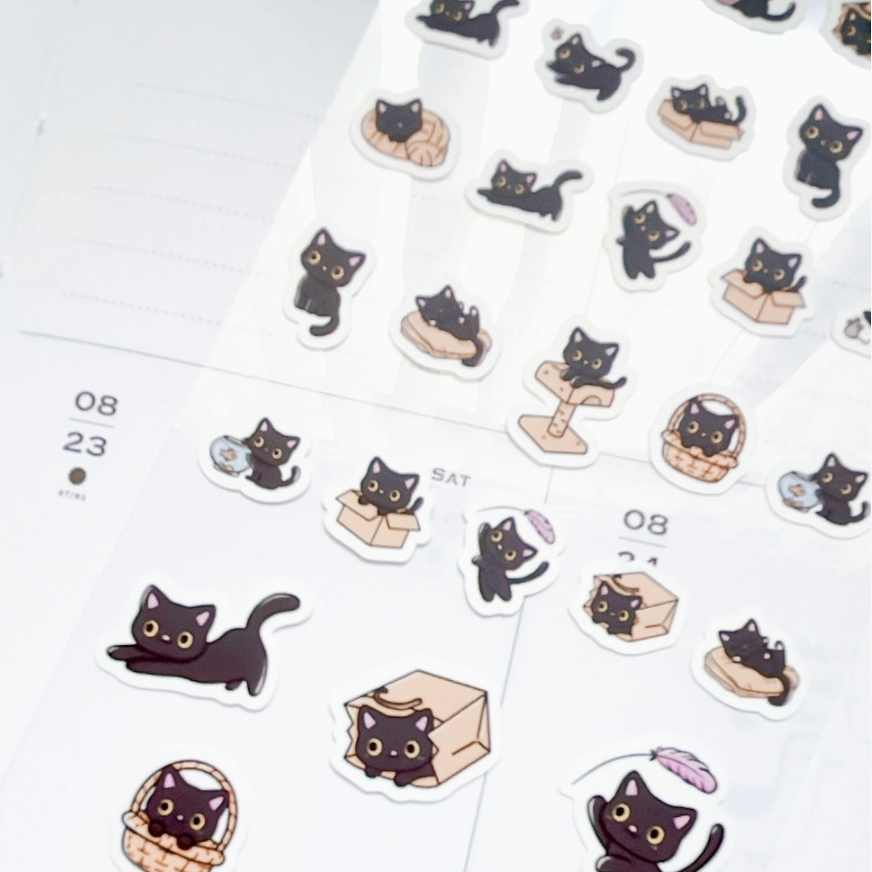 A sheet of cute die-cut stickers featuring black cats in various playful poses, displayed on a white planner page.