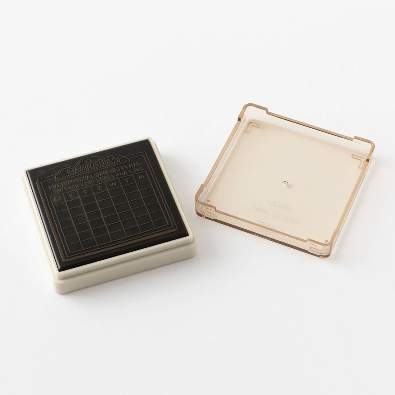 A square black-and-white calendar stamp with a transparent cover placed beside it on a white background.