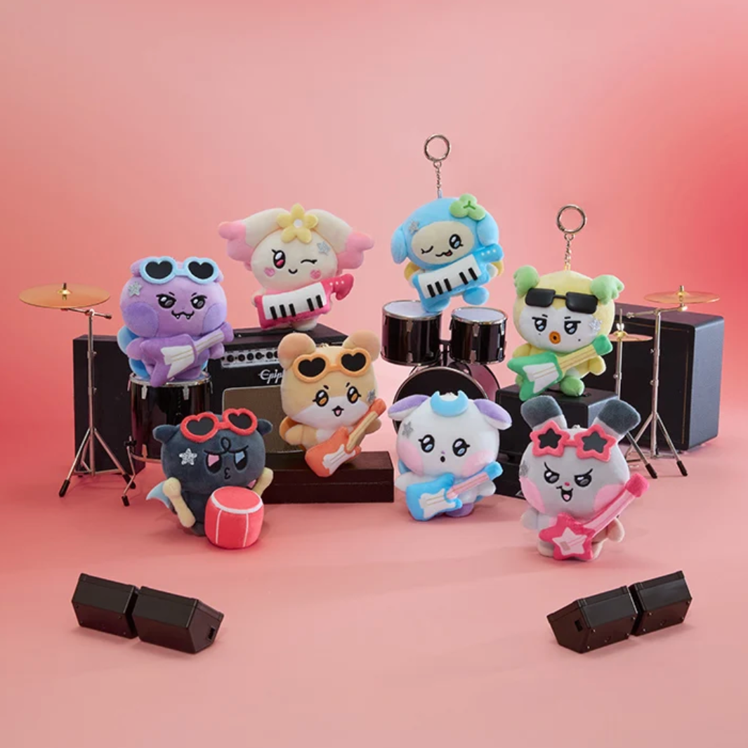 A group of nine colorful plush band characters arranged with toy drums, speakers, and microphones on a pink studio background. The characters wear sunglasses and each holds a different musical instrument, with no people or real environment present.