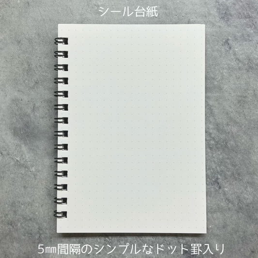 A white dotted sheet of paper with a black spiral binding, shown on a gray textured background with Japanese text above and below.