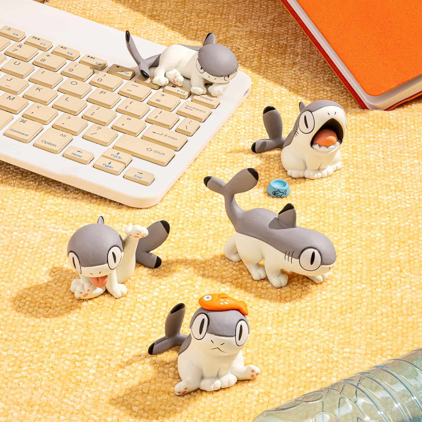 Small figurines resembling a shark and penguin on a desk with a keyboard and notebook.