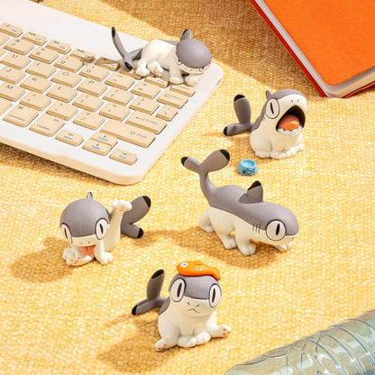 Small figurines resembling a shark and penguin on a desk with a keyboard and notebook.