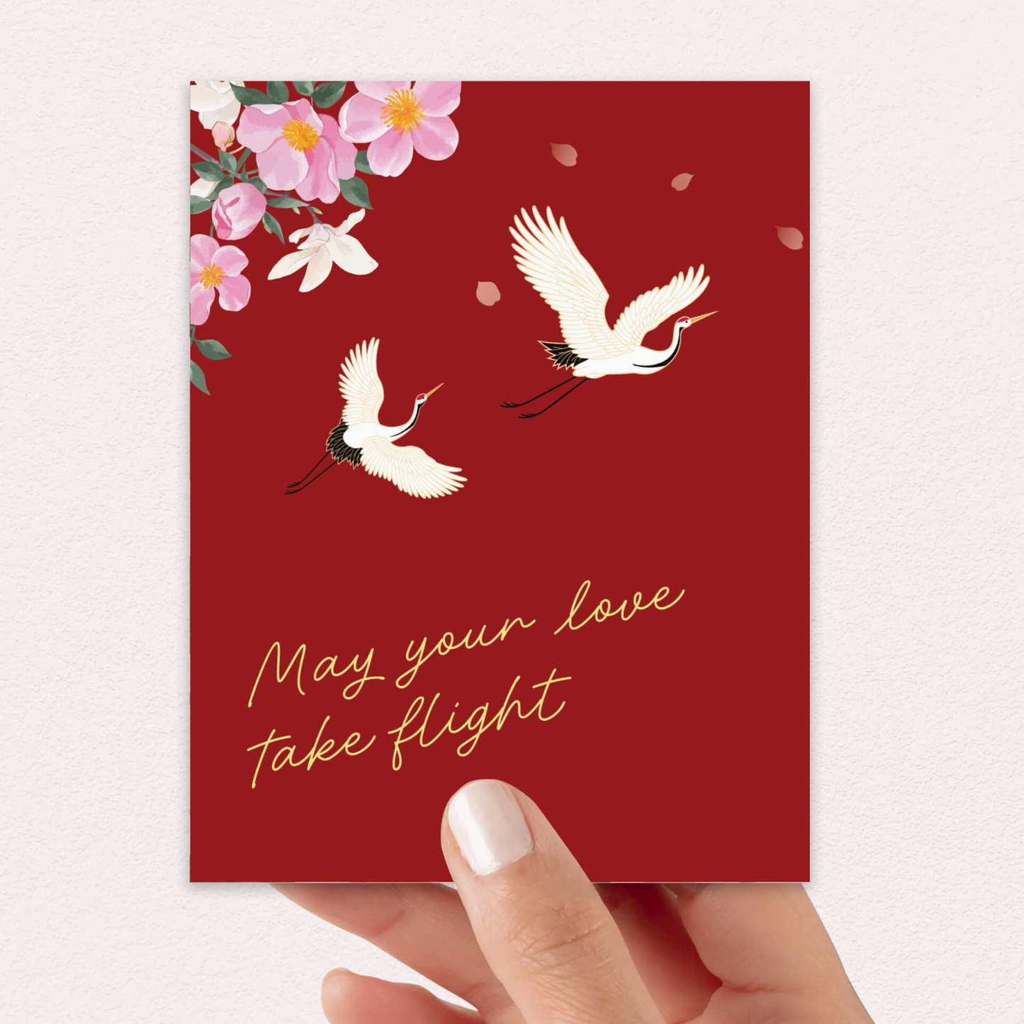 Red card with white cranes and flowers, featuring the text 'May your love take flight'.