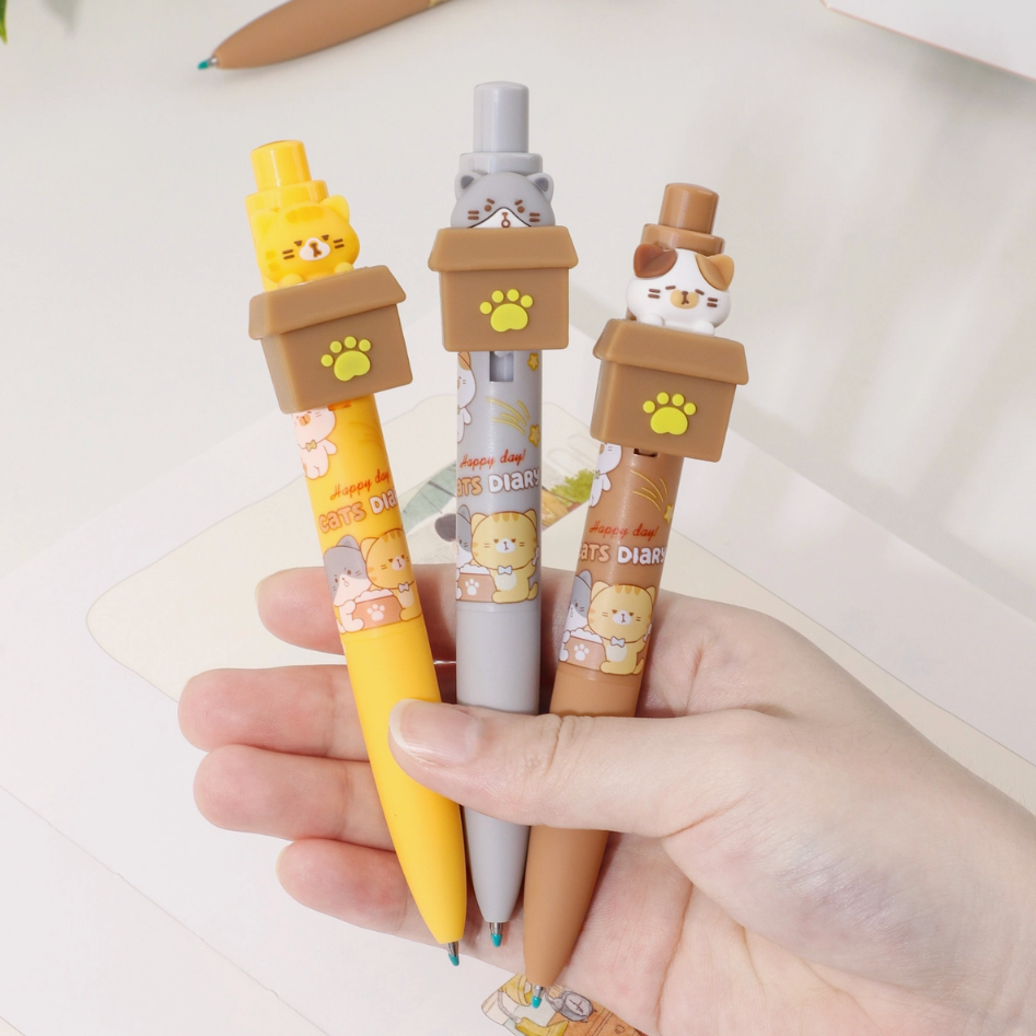 Hand holding three cartoon-style pens with cat-themed caps on a light background
