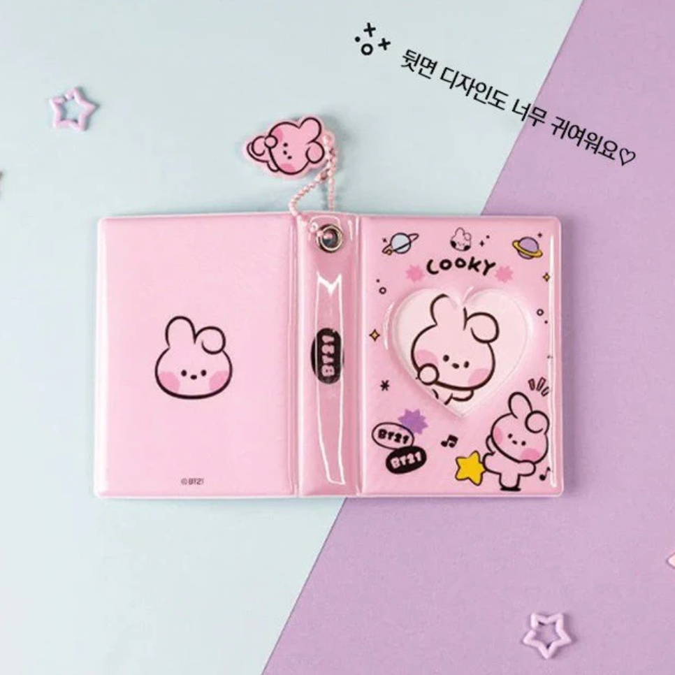 Pink photo album with heart window, and ball keychain with BT21 cartoon character 'COOKY' branding showing backside of album on a white background