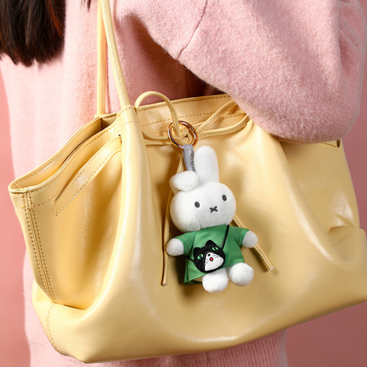Yellow handbag with a white bunny keychain featuring a black cat design, held by a person wearing a pink sweater.