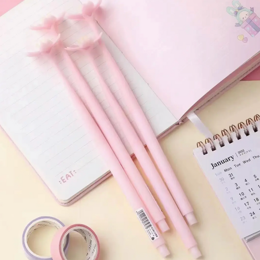 Set of pink pens on a desk with a notebook and calendar in the background