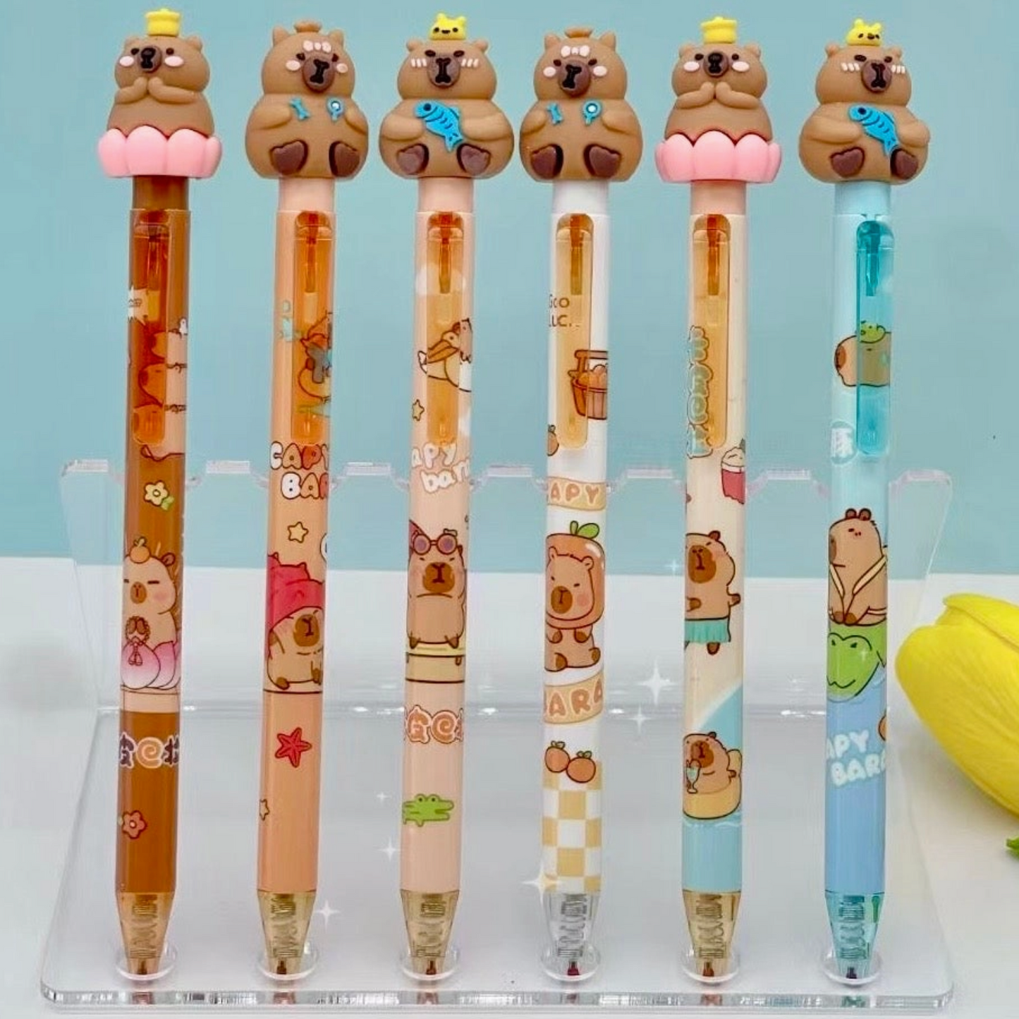 Set of cartoon capybara shaped pens on a clear stand with a light blue background