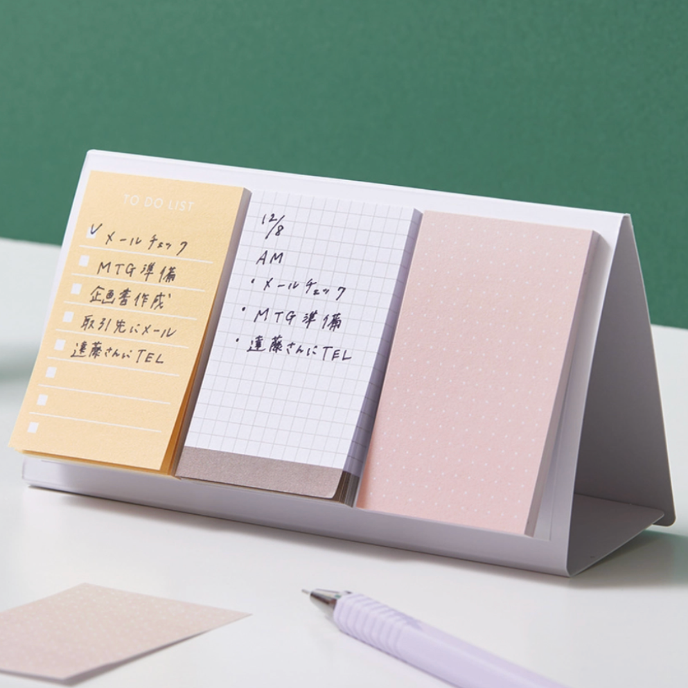 Desk organizer with sticky notes and a pen on a light surface with a green background