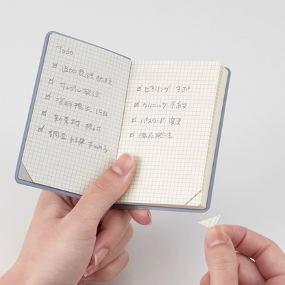 Small notebook with grid pages held by a hand on a light gray background