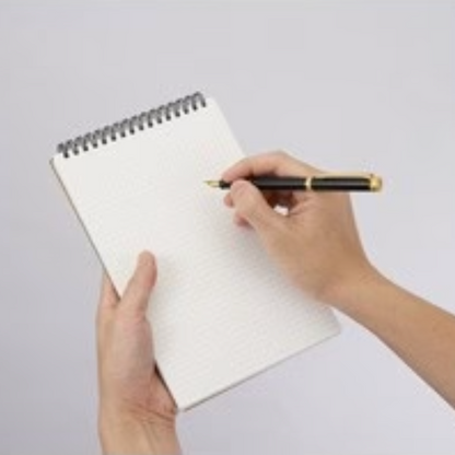 Hand holding a pen poised over a blank notebook on a light gray background
