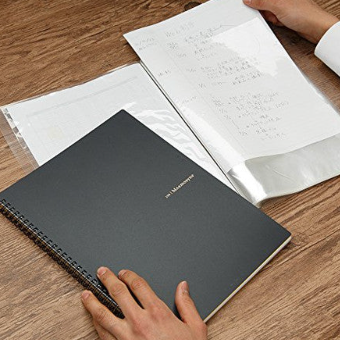 Person organizing documents with a black notebook on a wooden surface