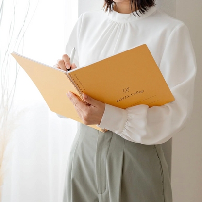 Person holding a yellow notebook with 'Royal College' branding against a plain background