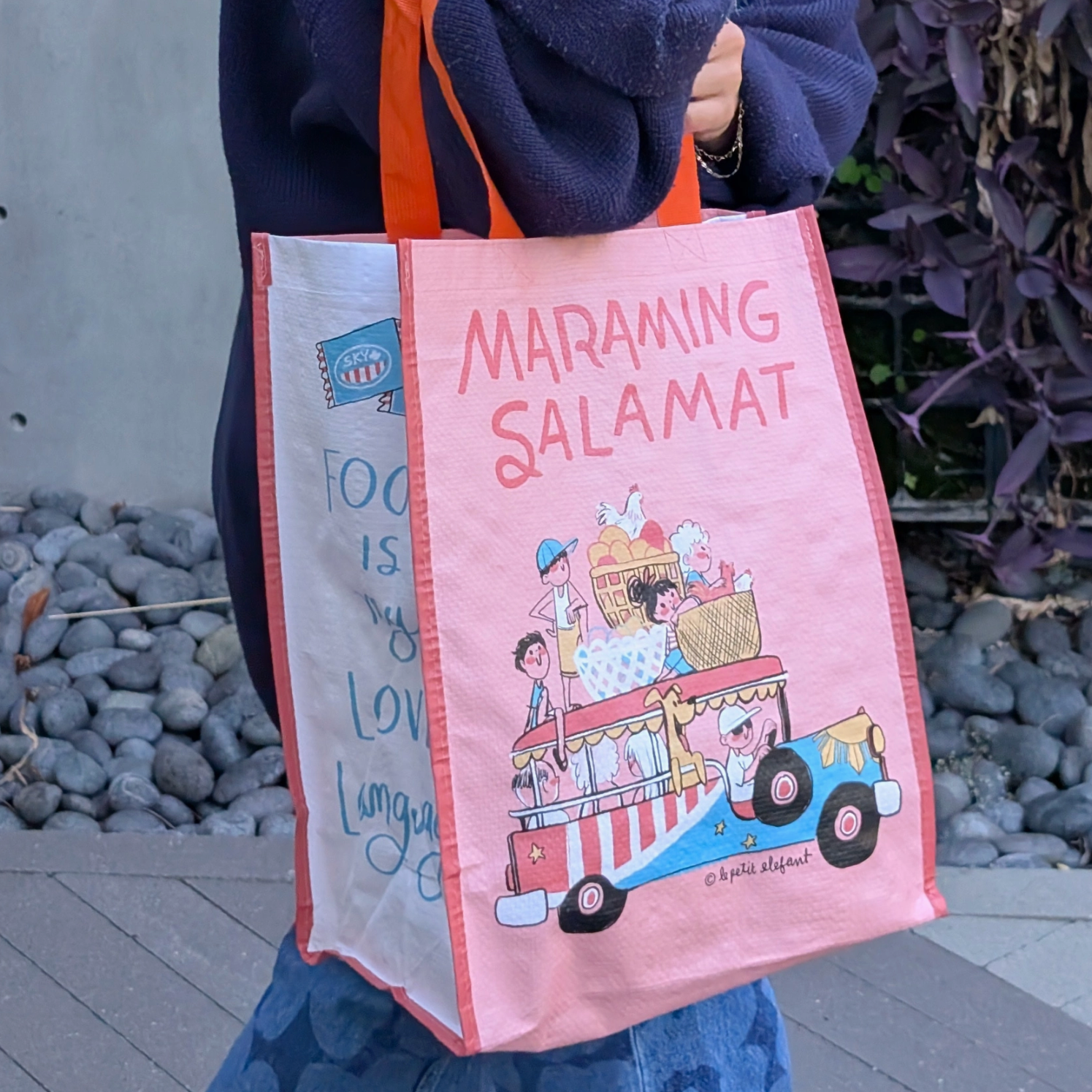 Person holding a pink tote bag with cartoon design and text.