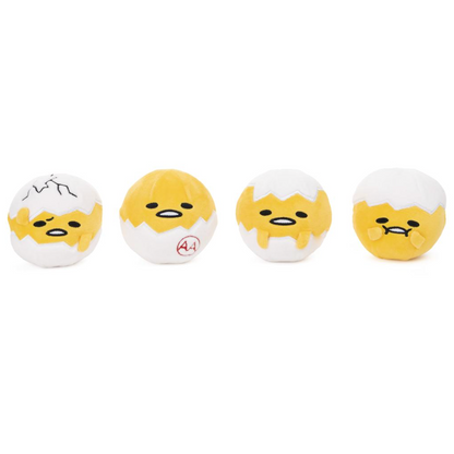 Four small plush egg-shaped toys lined up on a plain white background. Each toy has a yellow face and body peeking out from a white cracked eggshell, with different facial expressions and small red markings on some shells.