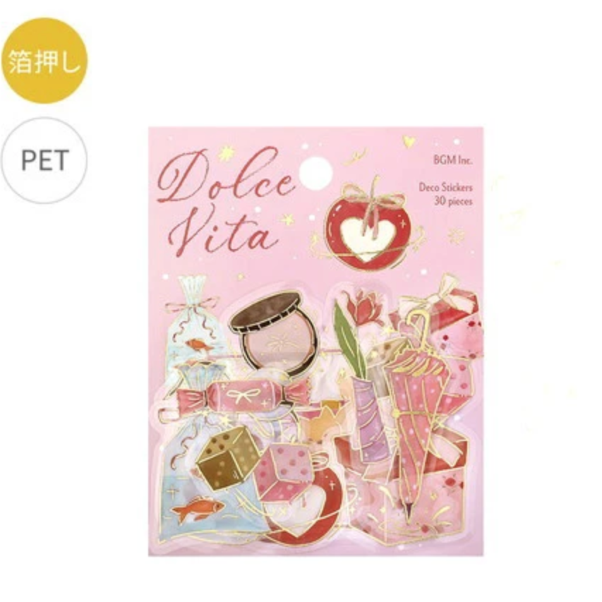 A pink package of 'Dolce Vita' dress stickers by BGM Inc., featuring retro candy and fashion illustrations on a white background with a yellow 'PET' label and a gold 'press' circle.