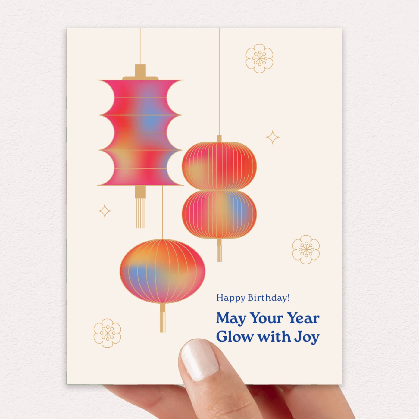 A hand holds a birthday card featuring a retro design with three colorful gradient lanterns and the text 'Happy Birthday! May Your Year Glow with Joy' against a light gray textured background.