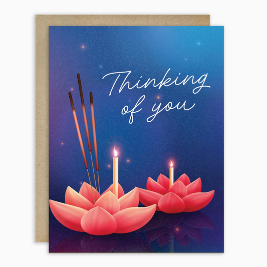 A greeting card with a kraft envelope, featuring a blue background with the words 'Thinking of you' in white script and illustrations of pink lotus flowers holding lit candles and incense sticks.