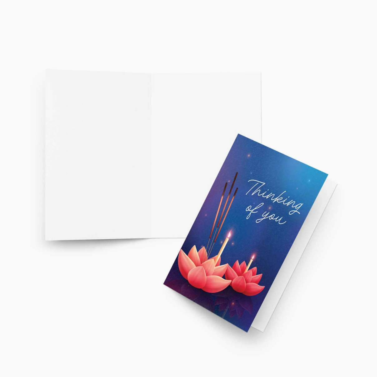 A folded greeting card with a blue and purple illustration of lotus flowers, candles, and incense sticks, next to an open blank white card on a light gray background.