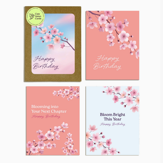 Four birthday cards arranged in a 2x2 grid on a light gray background. The cards feature pink and peach cherry blossom illustrations, with one card showing a gold envelope and a green circular 'One Card Magic' sticker.