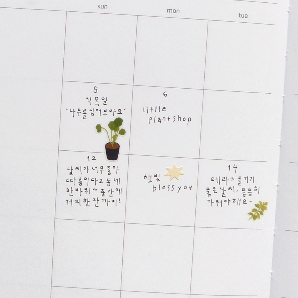 A white daily planner or calendar page with columns for sun through wed and handwritten notes in French and Korean, on white calendar background.
