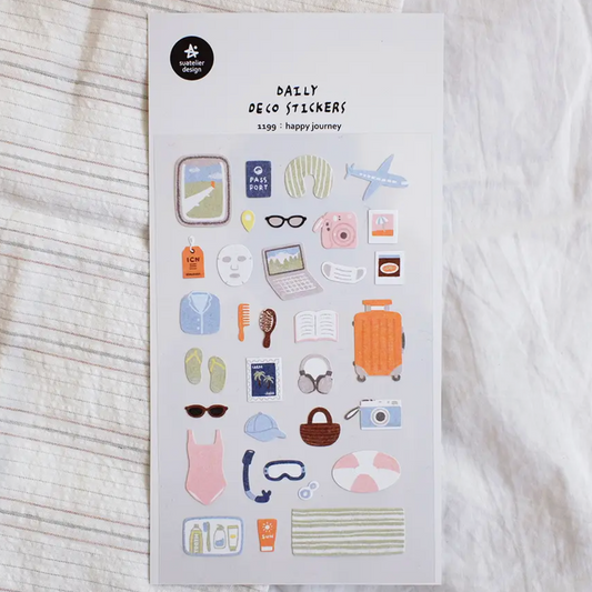A sheet of daily deco stickers featuring various travel and lifestyle icons like a suitcase, passport, sunglasses, and a laptop, displayed on a textured white fabric background.