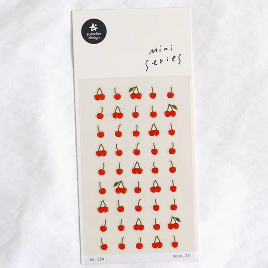 A sheet of cherry-themed mini stickers on a cream card, photographed flat on a white textured fabric background. The sheet features rows of small red cherries with green stems and handwritten text reading 'mini series' near the top.