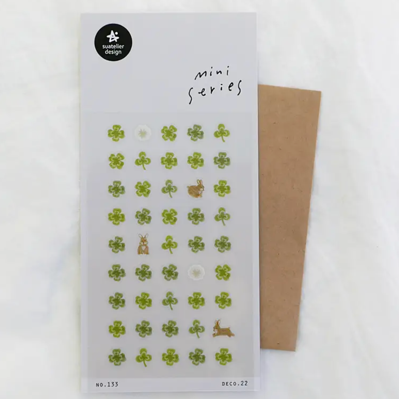 A sheet of small decorative stickers labeled 'mini series' with mostly green clover motifs and a few brown animal shapes, placed on a white background with a brown envelope behind it.