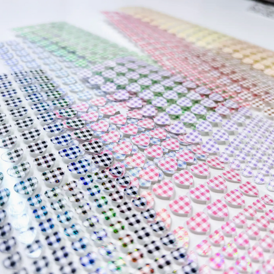 Multiple sheets of small heart-shaped adhesive stickers arranged diagonally, each printed with a different pastel gingham check pattern including pink, blue, green, purple, and yellow on a white background.