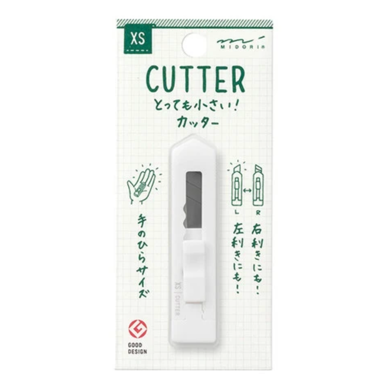 A white handheld paper cutter with a gray blade window, mounted on a white grid-patterned retail card with green text and illustrations. The card shows the brand MIDORI and size XS.