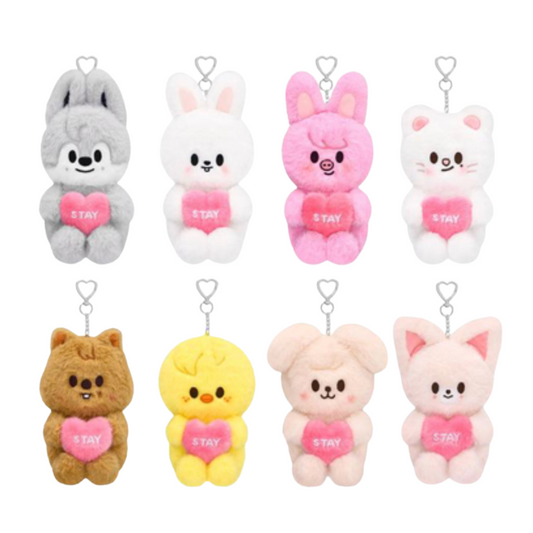 Eight small plush character keychain charms arranged in two rows on a plain white background. The characters include gray, white, pink, white, brown, yellow, pale pink, and light pink animals, each holding a pink heart that says "STAY" in white letters, with silver keychain loops above them.