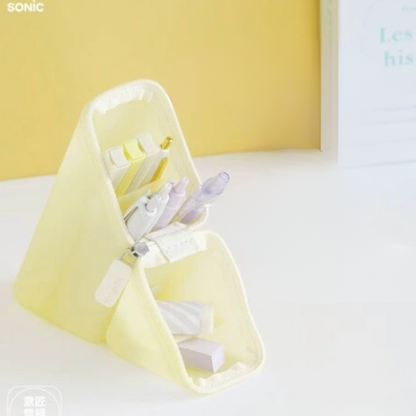 A pale yellow fabric desk organizer with multiple compartments holding pens and stationery, set on a white surface against a soft yellow background.