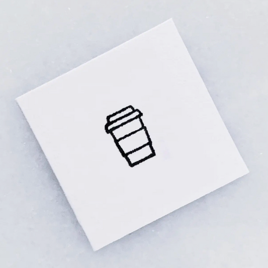 The top of a  white square stamp with a simple black line drawing of a takeaway coffee cup, photographed on a light gray background.