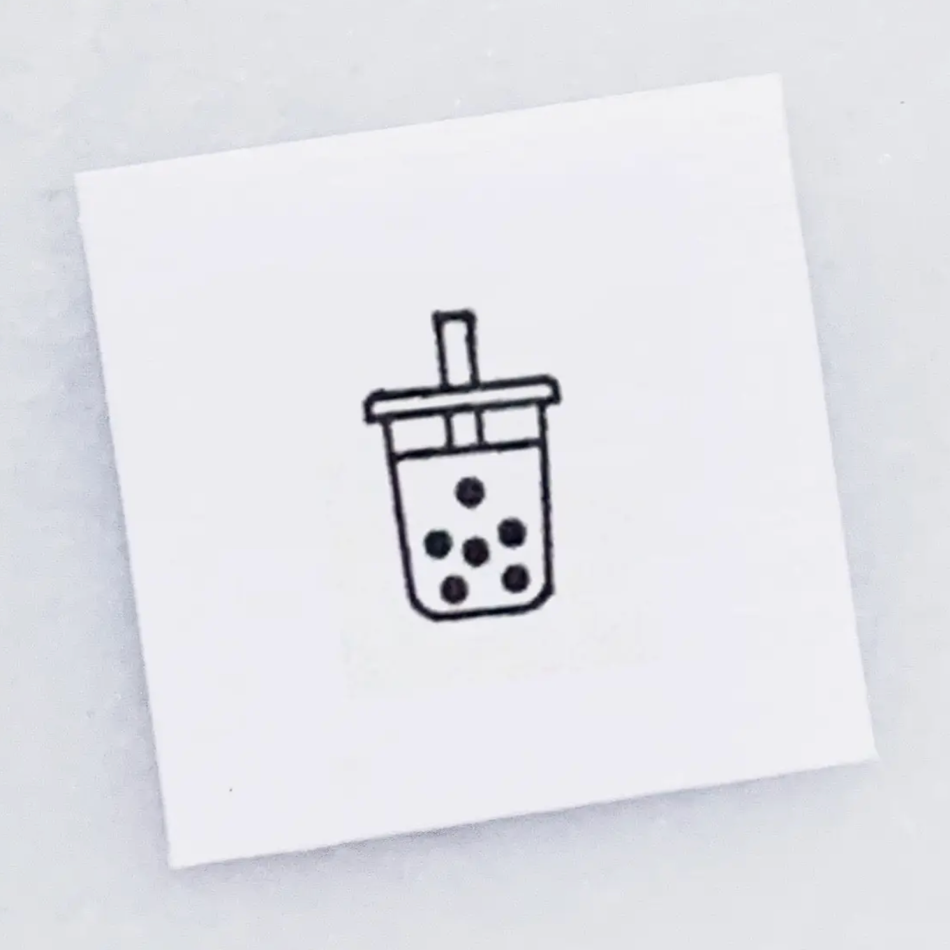 A square white card featuring a simple black line drawing of a boba tea cup with a straw, centered on a light gray background.