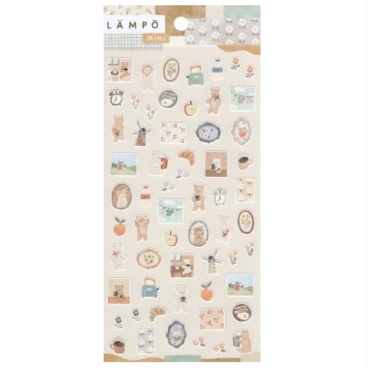 A sheet of mini decorative stickers with a cute, cozy aesthetic. The stickers feature illustrations of teddy bears, coffee cups, croissants, apples, and small scenes in muted pastel colors like beige, brown, orange, and blue, presented on a light cream backing card with the brand name 'LÄMPÖ MINI' visible at the top.