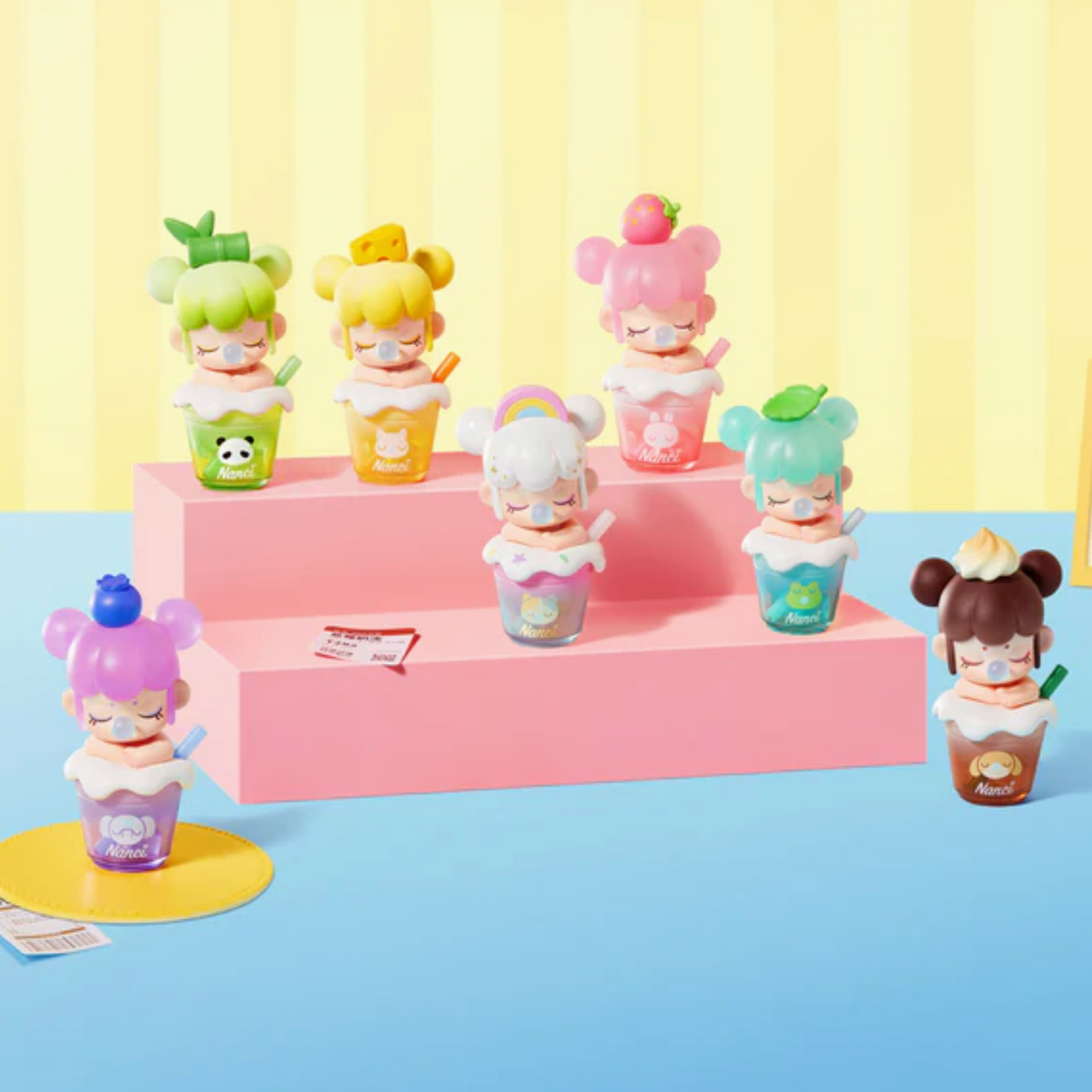 Six cute character figurines styled like milk tea drinks, each with a different hair color and fruit-themed cup, arranged on pink display steps against a pastel yellow and blue background.