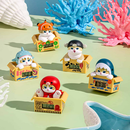 Six small cat figurines dressed as sea creatures sitting in yellow boxes, arranged on a mint green surface with coral and shell props.