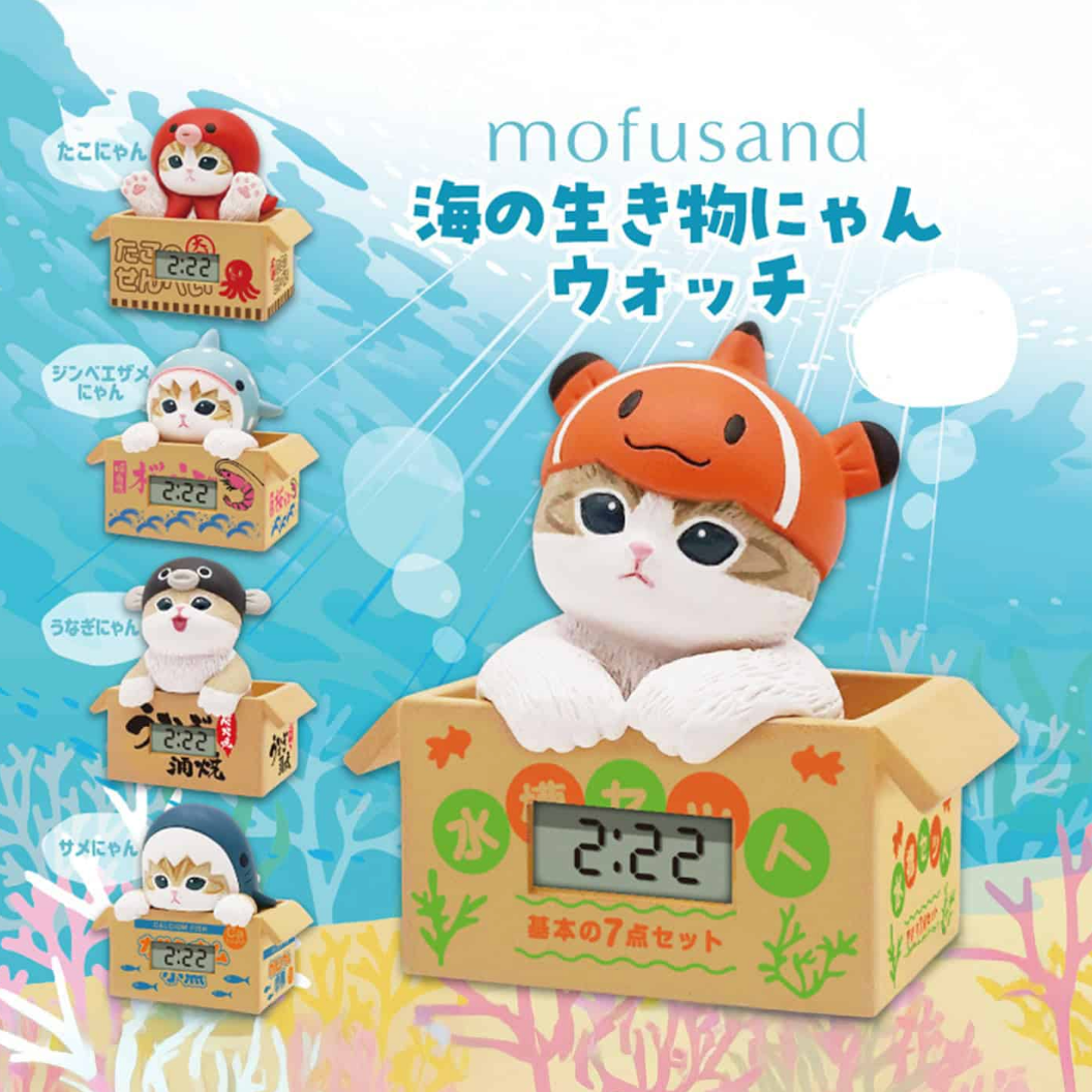 A set of five small cat figurines in cardboard boxes, each wearing a different sea creature hat, with a larger orange clownfish hat on the front box. The text 'mofusand' and Japanese text appear on a light blue underwater-themed background.