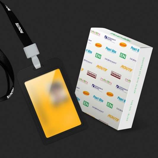 A black lanyard with a white clip holding a black ID badge holder containing a yellow card, shown next to a white branded box printed with ROUTE and EN logos, on a dark background.