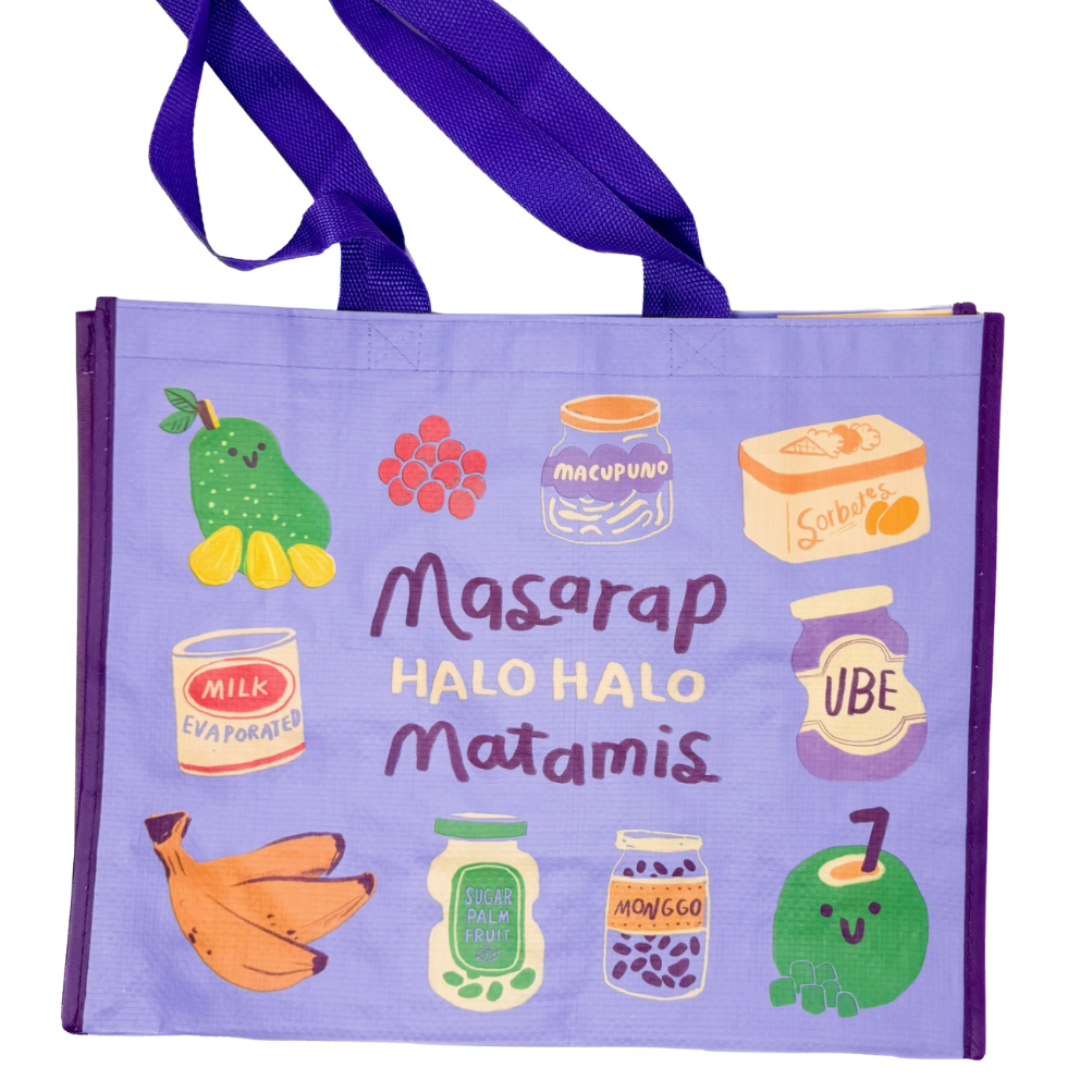 A light purple reusable tote bag with dark purple handles, decorated with cute illustrations of fruits and vegetables and the text 'Masaarap HALO HALO Matamis' on a white background.
