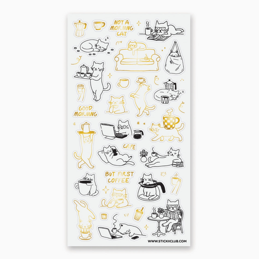 A sheet of clear adhesive stickers featuring cute hand-drawn illustrations of cats in various coffee-themed poses, accompanied by text like 'NOT A MORNING CAT' and 'GOOD MORNING' in black and gold outlines on a white backing sheet.